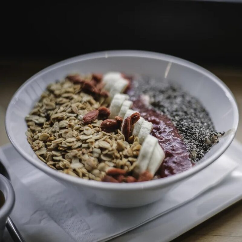 A white bowl of granola, banana slices, goji berries and chia.