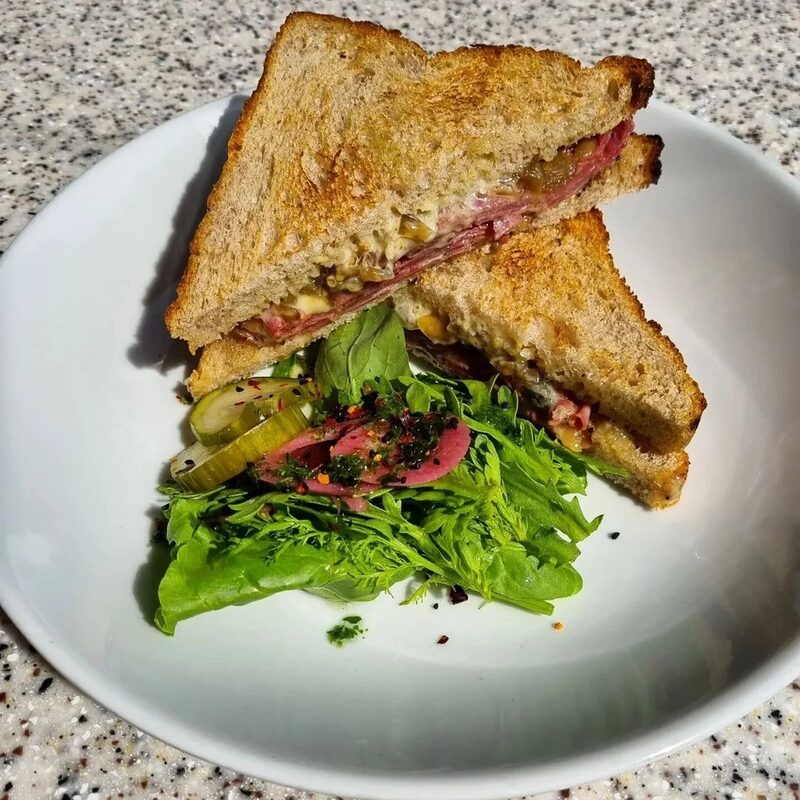A toasted sandwich cut in half beside a pile of dressed leaves and pickles.
