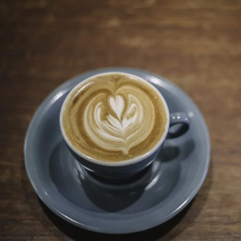 A flat white with latte art in a blue-grey cup on a wooden table.