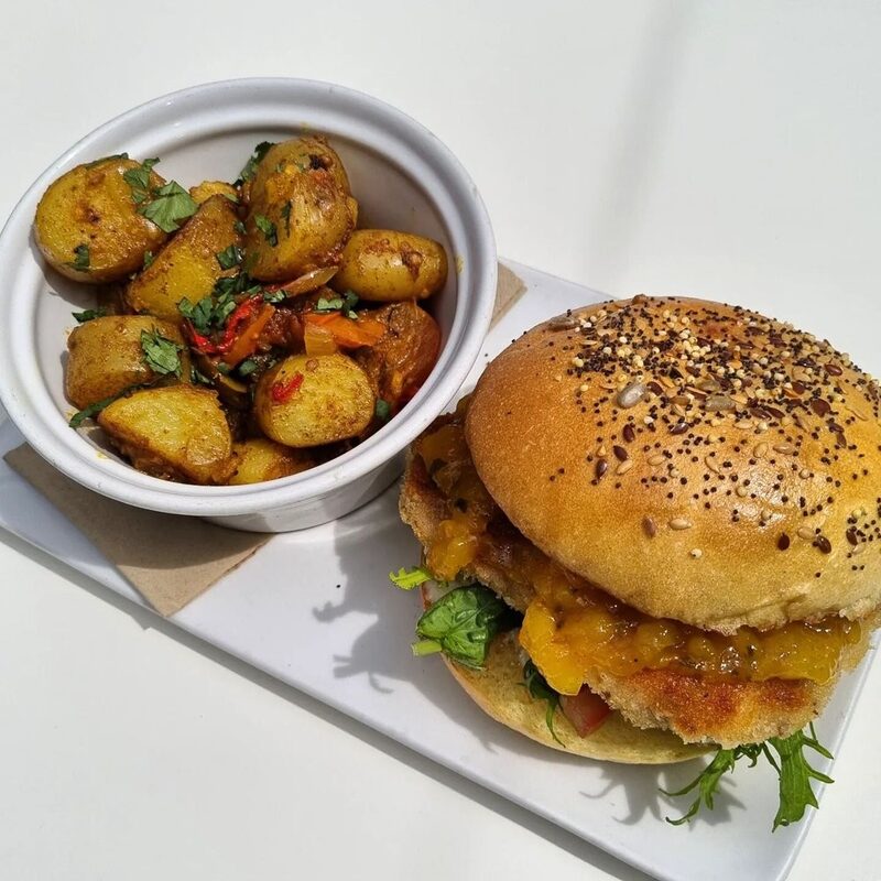 A seeded brioche roll beside a pot of roast potatoes.