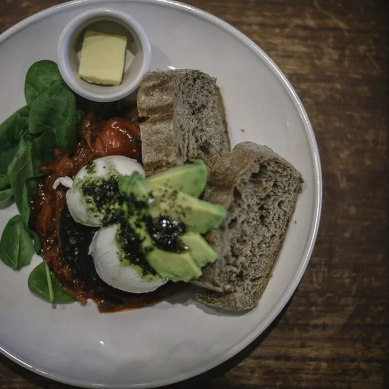 Poached eggs, avocado, tomato and sourdough on a white plate.